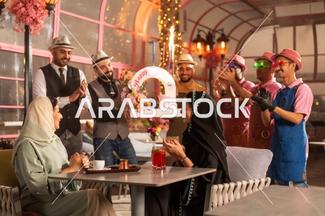 التزيين  للاحتفال بالمناسبات السعيدة، إقامة حفلات اعياد الميلاد في الكافيهات والمطاعم الفاخرة في المملكة، مشاركة طاقم الخدمة الاحتفال، قضاء وقت ممتع مع الأصدقاء، إيماءات السعادة والمفاجأة، امرأة عربية خليجية سعودية محجبة ترتدي العباءة تقوم بالاحتفال بعيد ميلاد صديقتها