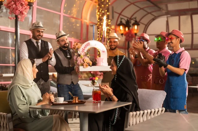 Decoration for celebrating happy occasions, holding birthday parties in cafes and luxury restaurants in the kingdom, sharing the celebration with the service staff, having a good time with friends, gestures of happiness and surprise, an Arab Gulf Saudi woman wearing a hijab and an abaya celebrating her friend's birthday.