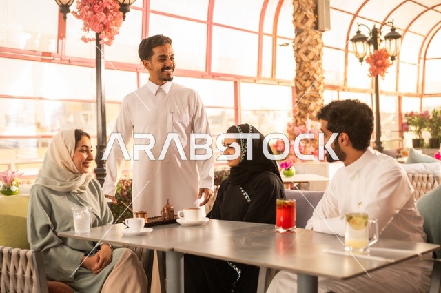 قضاء وقت ممتع في الخارج، الاستمتاع بتناول المشروبات الساخنة، حوارات ونقاشات عائلية، مفهوم الألفة والمحبة بين الأهل والأصدقاء, اصدقاء عرب خليجيون سعوديون يجلسون في احدى الكافيهات الراقية، ايماءات السعادة والسرور