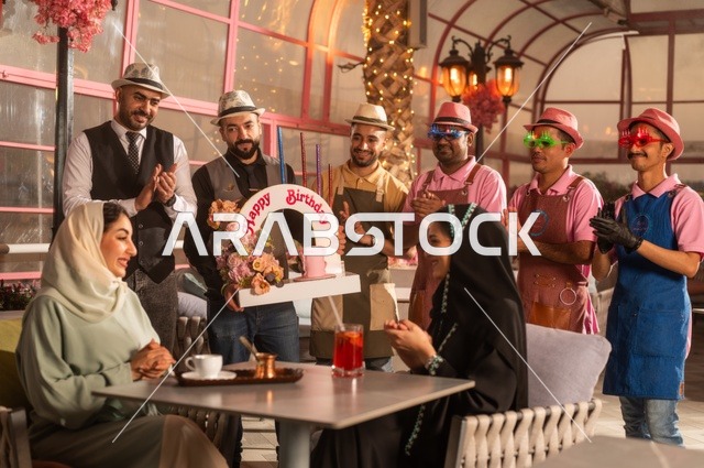 التزيين  للاحتفال بالمناسبات السعيدة، إقامة حفلات اعياد الميلاد في الكافيهات والمطاعم الفاخرة في المملكة، مشاركة طاقم الخدمة الاحتفال، قضاء وقت ممتع مع الأصدقاء، إيماءات السعادة والمفاجأة، امرأة عربية خليجية سعودية محجبة ترتدي العباءة تقوم بالاحتفال بعيد ميلاد صديقتها