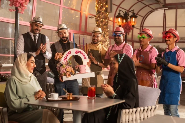 التزيين  للاحتفال بالمناسبات السعيدة، إقامة حفلات اعياد الميلاد في الكافيهات والمطاعم الفاخرة في المملكة، مشاركة طاقم الخدمة الاحتفال، قضاء وقت ممتع مع الأصدقاء، إيماءات السعادة والمفاجأة، امرأة عربية خليجية سعودية محجبة ترتدي العباءة تقوم بالاحتفال بعيد ميلاد صديقتها