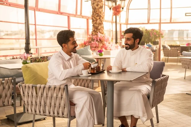 Building successful social relationships, exchanging conversations and news, sharing fun times with friends, enjoying hot coffee, two Saudi Arabian Gulf friends wearing traditional dress sitting in one of the luxurious cafes in the Kingdom