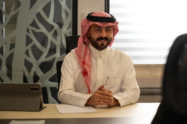 مهن ووظائف إدارية مكتبية للشباب في السعودية, دمج العمل مع التقنيات التكنولوجية، مفهوم العمل عن بعد عبر الانترنت، رجل عربي خليجي سعودي يرتدي الثوب التقليدي والشماغ يجلس خلف المكتب وأمامه جهاز التابلت
