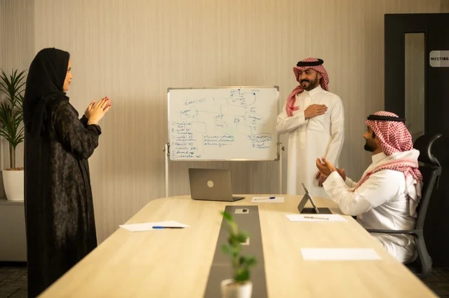 Gestures of encouragement and applause, using a laptop to take notes, ensuring a clear and comprehensive understanding of the work, using a whiteboard to clarify the processes and procedures followed in the company, teamwork and team spirit, professionalism and dedication to achievement, a Saudi Gulf Arab team in a meeting inside the office.