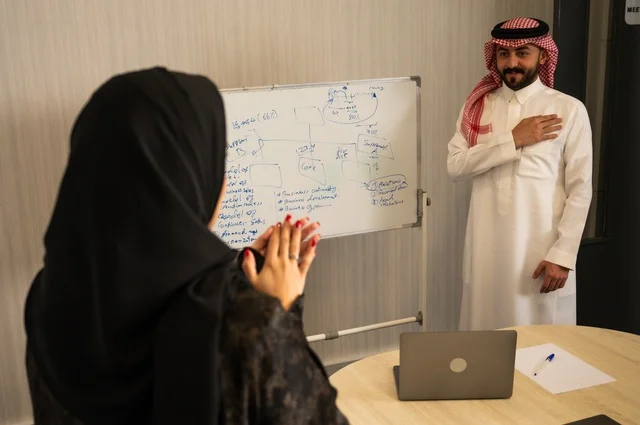 Gestures of encouragement and applause, using a laptop to take notes, ensuring a clear and comprehensive understanding of the work, using a whiteboard to clarify the processes and procedures followed in the company, teamwork and team spirit, professionalism and dedication to achievement, a Saudi Gulf Arab team in a meeting inside the office.