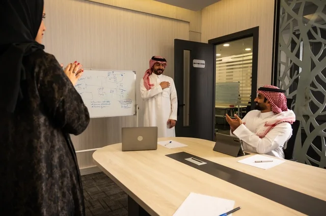 Gestures of encouragement and applause, using a laptop to take notes, ensuring a clear and comprehensive understanding of the work, using a whiteboard to clarify the processes and procedures followed in the company, teamwork and team spirit, professionalism and dedication to achievement, a Saudi Gulf Arab team in a meeting inside the office.