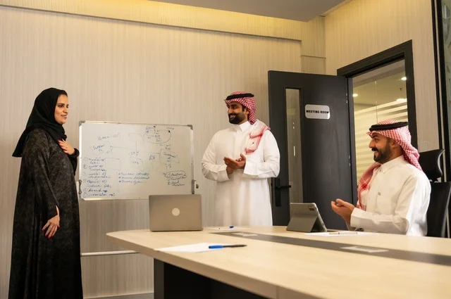 Gestures of encouragement and applause, using a laptop to take notes, ensuring a clear and comprehensive understanding of the work, using a whiteboard to clarify the processes and procedures followed in the company, teamwork and team spirit, professionalism and dedication to achievement, a Saudi Gulf Arab team in a meeting inside the office.