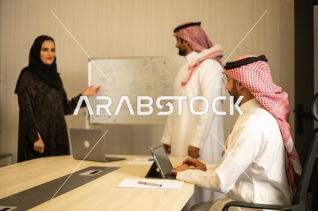 Using the whiteboard to clarify the processes and procedures followed in the company, teamwork and team spirit, discussing work plans, using the laptop to take notes, professionalism and dedication to achievement, a Saudi Gulf Arab team in a meeting inside the office, ensuring a clear and comprehensive understanding of the work.