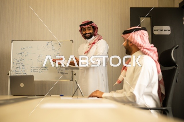 استعمال السبورة لتوضيح العمليات والاجراءات المتبعة في الشركة، العمل الجماعي وروح الفريق، مناقشة خطط العمل، استخدام اللابتوب في تدوين الملاحظات، الاحترافية والتفاني في الإنجاز، فريق عربي خليجي سعودي في اجتماع داخل المكتب، ضمان فهم واضح وشامل للاعمال