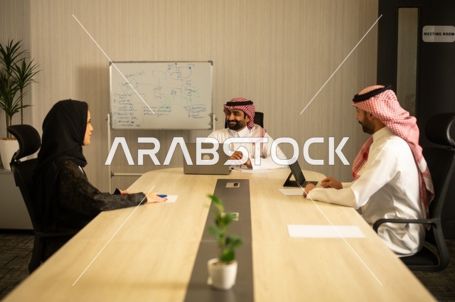Using the whiteboard to clarify the processes and procedures followed in the company, teamwork and team spirit, discussing work plans, using the laptop to take notes, professionalism and dedication to achievement, a Saudi Gulf Arab team in a meeting inside the office, ensuring a clear and comprehensive understanding of the work.