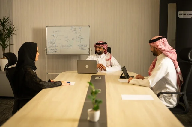 Using the whiteboard to clarify the processes and procedures followed in the company, teamwork and team spirit, discussing work plans, using the laptop to take notes, professionalism and dedication to achievement, a Saudi Gulf Arab team in a meeting inside the office, ensuring a clear and comprehensive understanding of the work.