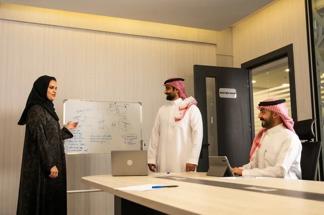 Using the whiteboard to clarify the processes and procedures followed in the company, teamwork and team spirit, discussing work plans, using the laptop to take notes, professionalism and dedication to achievement, a Saudi Gulf Arab team in a meeting inside the office, ensuring a clear and comprehensive understanding of the work.