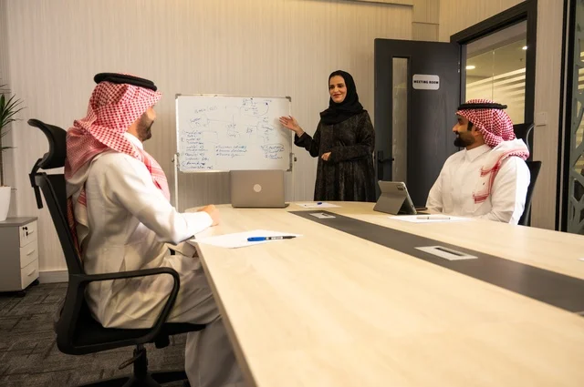 Teamwork and team spirit, discussing work plans, using laptops to take notes, professionalism and dedication to achievement, a Saudi Gulf Arab team in a meeting inside the office, ensuring a clear and comprehensive understanding of the work, clarifying the processes and procedures followed in the company.