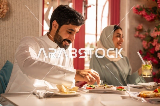 تبادل الأحاديث والاخبار, مشاركة الأصدقاء الأوقات الممتعة, الاستمتاع بتناول الغداء في المطعم, جلسة وناسة وتعارف، بناء علاقات اجتماعية ناجحة, عائلة عرب خليجيون سعوديون يجلسون على المائدة في إحدى المطاعم الراقية ويقومون بتناول الطعام بإيماءات السعادة والسرور