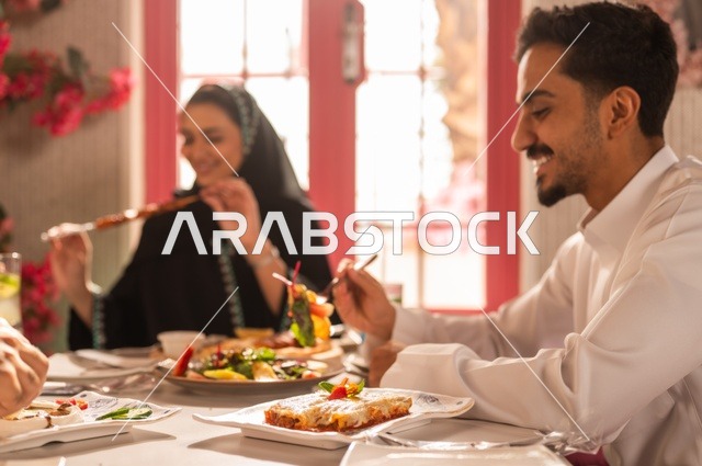 تبادل الأحاديث والاخبار, مشاركة الأصدقاء الأوقات الممتعة, الاستمتاع بتناول الغداء في المطعم, جلسة وناسة وتعارف، بناء علاقات اجتماعية ناجحة, عائلة عرب خليجيون سعوديون يجلسون على المائدة في إحدى المطاعم الراقية ويقومون بتناول الطعام بإيماءات السعادة والسرور