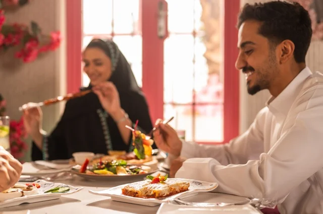 تبادل الأحاديث والاخبار, مشاركة الأصدقاء الأوقات الممتعة, الاستمتاع بتناول الغداء في المطعم, جلسة وناسة وتعارف، بناء علاقات اجتماعية ناجحة, عائلة عرب خليجيون سعوديون يجلسون على المائدة في إحدى المطاعم الراقية ويقومون بتناول الطعام بإيماءات السعادة والسرور