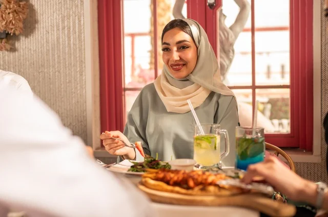 تبادل الأحاديث والاخبار, مشاركة الأصدقاء الأوقات الممتعة, الاستمتاع بتناول الغداء في المطعم, جلسة وناسة وتعارف، بناء علاقات اجتماعية ناجحة, عائلة عرب خليجيون سعوديون يجلسون على المائدة في إحدى المطاعم الراقية ويقومون بتناول الطعام بإيماءات السعادة والسرور