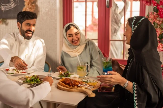 A fun and social gathering, building successful social relationships, exchanging conversations and news, sharing enjoyable moments with friends, enjoying lunch at a restaurant, a family of Saudi Gulf Arabs sitting at the table in one of the upscale restaurants and eating with gestures of happiness and joy.