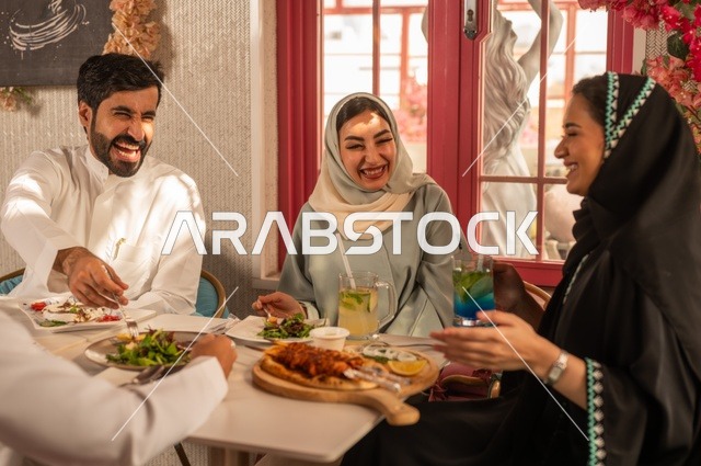 A fun and social gathering, building successful social relationships, exchanging conversations and news, sharing enjoyable moments with friends, enjoying lunch at a restaurant, a family of Saudi Gulf Arabs sitting at the table in one of the upscale restaurants and eating with gestures of happiness and joy.