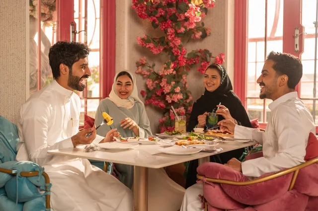 Enjoying lunch at the restaurant, a fun and social gathering, building successful social relationships, exchanging conversations and news, sharing enjoyable moments with friends, a family of Gulf Arab Saudis sitting at the table in one of the upscale restaurants, eating with gestures of happiness and joy.