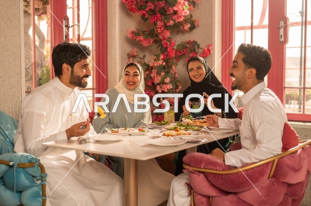 A fun and social gathering, building successful social relationships, exchanging conversations and news, sharing enjoyable moments with friends, enjoying lunch at a restaurant, a family of Saudi Gulf Arabs sitting at the table in one of the upscale restaurants and eating with gestures of happiness and joy.