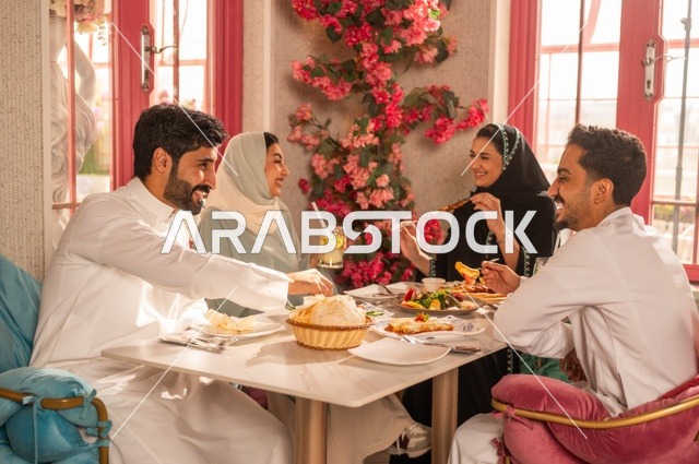Exchanging conversations and news, sharing enjoyable times with friends, enjoying lunch at a restaurant, a fun and social gathering, building successful social relationships, a family of Saudi Gulf Arabs sitting at the table in one of the upscale restaurants and eating with gestures of happiness and joy.