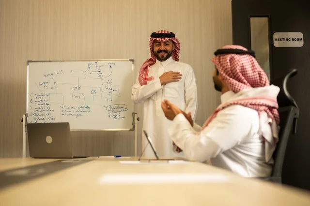 تبادل الخبرات والافكار، دراسة وتحليل المشاريع الجديدة، استخدام جهاز تقني حديث، الوحدة والعمل الجماعي، تطوير العمل وحل المشكلات، رجل عربي خليجي سعودي يرتدي الشماغ والثوب التقليدي يقوم بالعمل برفقة مديره، مهنة ووظيفة سعودية مكتبية