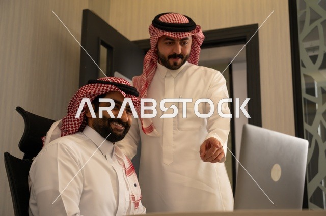 تبادل الخبرات والافكار، دراسة وتحليل المشاريع الجديدة، استخدام جهاز تقني حديث، الوحدة والعمل الجماعي، تطوير العمل وحل المشكلات، رجل عربي خليجي سعودي يرتدي الشماغ والثوب التقليدي يقوم بالعمل برفقة مديره، مهنة ووظيفة سعودية مكتبية