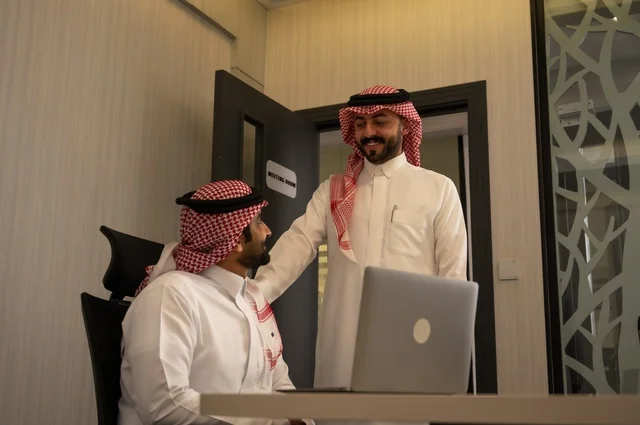 تبادل الخبرات والافكار، دراسة وتحليل المشاريع الجديدة، استخدام جهاز تقني حديث، الوحدة والعمل الجماعي، تطوير العمل وحل المشكلات، رجل عربي خليجي سعودي يرتدي الشماغ والثوب التقليدي يقوم بالعمل برفقة مديره، مهنة ووظيفة سعودية مكتبية