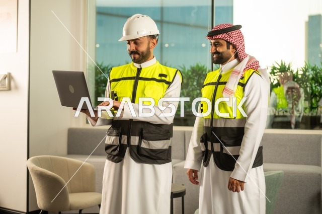 الشركات المختصة بورشات البناء والمقاولات، تصميم وتخطيط المخططات المعمارية عبر الحاسوب المحمول، متابعة تنفيذ الخطط الهندسية، رجلان مهندسان عربيان خليجيان سعوديان يرتدي زي العمل يقومان بالمناقشة وتبادل الخبرات، استخدام جهاز تقني حديث