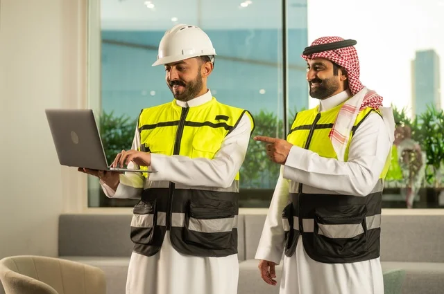 Companies specialized in construction workshops and contracting, designing and planning architectural plans using a laptop, monitoring the implementation of engineering plans, two Arab Gulf engineers from Saudi Arabia in work attire discussing and exchanging experiences, using modern technical devices.