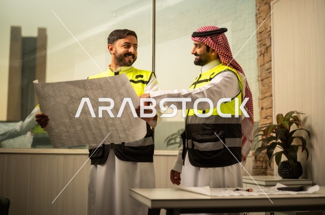Monitoring the implementation of engineering plans, companies specialized in construction workshops and contracting, planning and establishing the fundamentals of architectural designs, two Saudi Gulf Arab engineers wearing safety vests are discussing the construction plan and accurately determining the measurements.