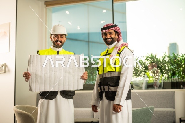 متابعة تنفيذ الخطط الهندسية، الشركات المختصة بورشات البناء والمقاولات، التخطيط ووضع اساسيات المخططات المعمارية، مهندسان عربيان خليجيان سعوديان يرتديان سترة الحماية يعملان على مناقشة مخطط الإنشاء وتحديد القياسات بدقة