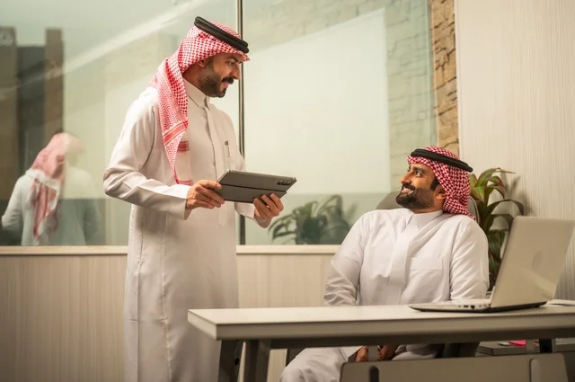 تبادل الخبرات والافكار، دراسة وتحليل المشاريع الجديدة، استخدام جهاز تقني حديث، الوحدة والعمل الجماعي، تطوير العمل وحل المشكلات، رجل عربي خليجي سعودي يرتدي الشماغ والثوب التقليدي يقوم بالعمل برفقة مديره، مهنة ووظيفة سعودية مكتبية