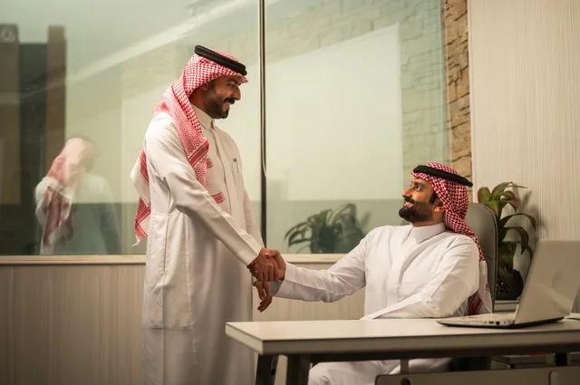 تبادل الخبرات والافكار، دراسة وتحليل المشاريع الجديدة، استخدام جهاز تقني حديث، الوحدة والعمل الجماعي، تطوير العمل وحل المشكلات، رجل عربي خليجي سعودي يرتدي الشماغ والثوب التقليدي يقوم بالعمل برفقة مديره، مهنة ووظيفة سعودية مكتبية