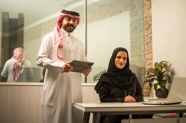 تعليم الموظفين الأساليب الجديدة في العمل لتحقيق أهداف الشركة، دمج العمل مع التقنية والتكنولوجيا، زميلان عربيان خليجيان سعوديان يقومان بإنجاز المهام عبر الحاسوب المحمول والتابلت، العمل الجماعي وروح الفريق الواحد