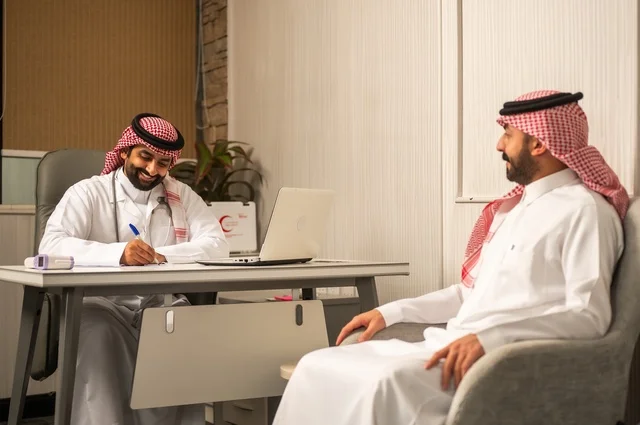 متابعة السجل الطبي للمراجعين, تسجيل حالات المرضى على جهاز الحاسوب, طبيب عربي خليجي سعودي يرتدي المعطف الأبيض يقوم بشرح الحالة المرضية لمريض يرتدي الشماغ والثوب التقليدي، الحوار مع المرضى لكشف الحالة، تقديم الاستشارات في المراكز الطبيه, العمل في القطاعات الصحية