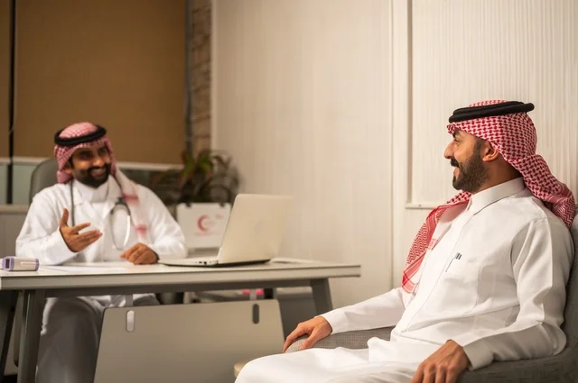Monitoring the medical records of patients, recording patient cases on the computer, an Arab Gulf Saudi doctor wearing a white coat explaining the medical condition to a patient wearing a ghutrah and traditional thobe, dialogue with patients to uncover the condition, providing consultations in medical centers, working in the health sectors.