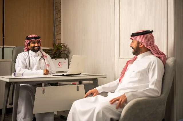 متابعة السجل الطبي للمراجعين, تسجيل حالات المرضى على جهاز الحاسوب, طبيب عربي خليجي سعودي يرتدي المعطف الأبيض يقوم بشرح الحالة المرضية لمريض يرتدي الشماغ والثوب التقليدي، الحوار مع المرضى لكشف الحالة، تقديم الاستشارات في المراكز الطبيه, العمل في القطاعات الصحية