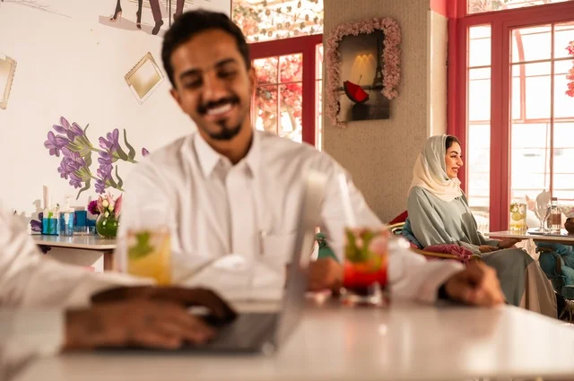 استخدام التكنولوجيا في الحياة اليومية، جلسة تسلية وترفيه شبابية، تناول المشروبات الباردة،  صداقة وتعارف وبناء علاقات، ايماءات السعادة والسرور، صورة مقربة لشابان عربيان خليجيان سعوديان يرتديان الثوب الأبيض يجلسان في كوفي شوب راقي، قضاء وقت ممتع في الخارج