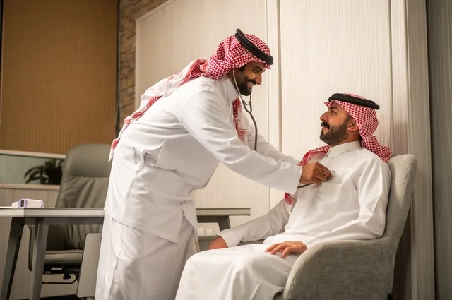 قياس  معدل ضربات القلب, مفهوم الطب والرعاية الصحية, المتابعة الدورية لفحص نبضات القلب, طبيب عربي خليجي سعودي يرتدي المعطف الطبي يقوم باستخدام سماعه الفحص الطبية لمريض يرتدي الشماغ والثوب التقليدي