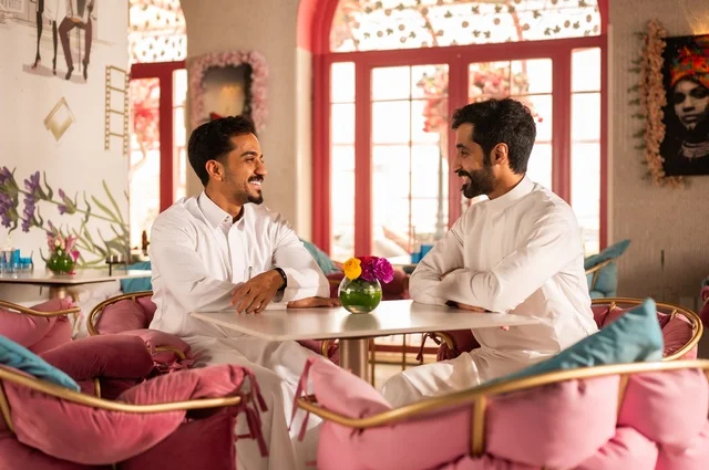 تبادل الأحاديث والحوار بين الأصدقاء، جلسة تسلية وترفيه شبابية، تبادل أطراف الحديث، صداقة وتعارف وبناء علاقات، ايماءات السعادة والسرور، شابان عربيان خليجيان سعوديان يرتديان الثوب الأبيض يجلسان في كوفي شوب راقي، قضاء وقت ممتع في الخارج