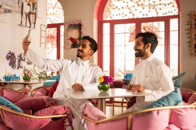التقاط سيلفي تذكاري لللحظات الجميلة مع الأصدقاء، جلسة تسلية وترفيه شبابية، تبادل أطراف الحديث، صداقة وتعارف وبناء علاقات، ايماءات السعادة والسرور، شابان عربيان خليجيان سعوديان يرتديان الثوب الأبيض يجلسان في كوفي شوب راقي، قضاء وقت ممتع في الخارج