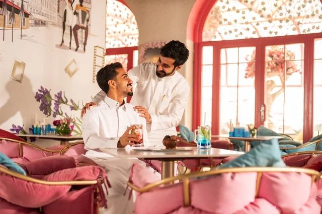Facial expressions of smiles and affection, enjoying cold drinks, a session of youthful entertainment and fun, friendship and acquaintance and building relationships, gestures of happiness and joy, two young Arab Gulf Saudis wearing white thobes sitting in an upscale coffee shop, spending enjoyable time outdoors.