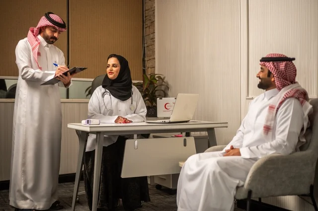 مفهوم الطب والرعاية الصحية، طبيبة عربية خليجية سعودية محجبة ترتدي العباءة مع المعطف الابيض تقوم بتسجيل حالة المرضى برفقة مساعدها، مهنة ووظيفة نسائية، تقديم الخدمات الصحية للمريض، العمل في القطاع الصحي في المملكة