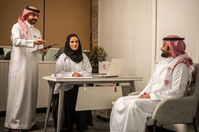 مفهوم الطب والرعاية الصحية، طبيبة عربية خليجية سعودية محجبة ترتدي العباءة مع المعطف الابيض تقوم بتسجيل حالة المرضى برفقة مساعدها، مهنة ووظيفة نسائية، تقديم الخدمات الصحية للمريض، العمل في القطاع الصحي في المملكة