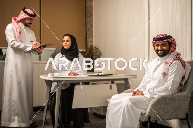مفهوم الطب والرعاية الصحية، طبيبة عربية خليجية سعودية محجبة ترتدي العباءة مع المعطف الابيض تقوم بتسجيل حالة المرضى برفقة مساعدها، مهنة ووظيفة نسائية، تقديم الخدمات الصحية للمريض، العمل في القطاع الصحي في المملكة