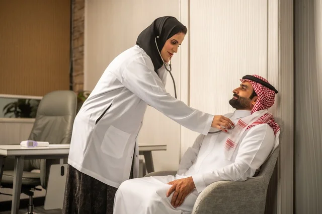 قياس  معدل ضربات القلب, مفهوم الطب والرعاية الصحية, المتابعة الدورية لفحص نبضات القلب, طبيب عربي خليجي سعودي يرتدي المعطف الطبي يقوم باستخدام سماعه الفحص الطبية لمريض يرتدي الشماغ والثوب التقليدي