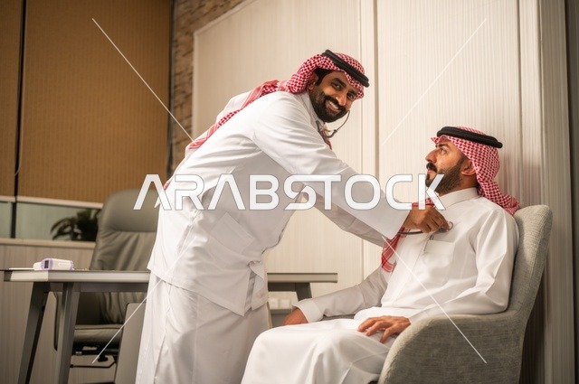 قياس  معدل ضربات القلب, مفهوم الطب والرعاية الصحية, المتابعة الدورية لفحص نبضات القلب, طبيب عربي خليجي سعودي يرتدي المعطف الطبي يقوم باستخدام سماعه الفحص الطبية لمريض يرتدي الشماغ والثوب التقليدي