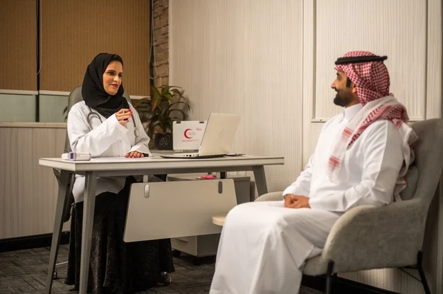 تقديم الاستشارات في المراكز الطبيه, العمل في القطاعات الصحية، متابعة السجل الطبي للمراجعين, تسجيل حالات المرضى على جهاز الحاسوب, طبيبة عربية خليجية سعودية ترتدي المعطف الأبيض تقوم بشرح الحالة المرضية لمريض يرتدي الشماغ والثوب التقليدي، الحوار مع المرضى لكشف الحالة